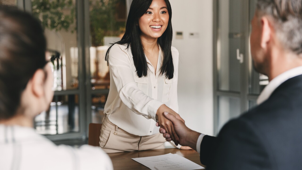 Two managers shake the hand of a young Asian woman in a conference room.