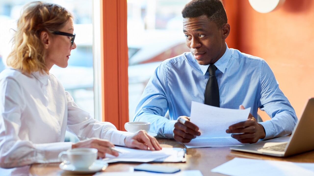 Two employees talking, sitting at table, looking at papers