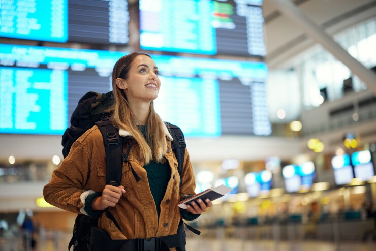 Woman standing in airport holding phone with backpack