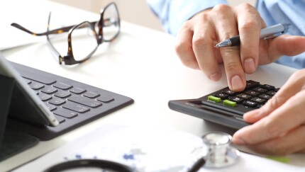 A man using a calculator sitting in front of a laptop.