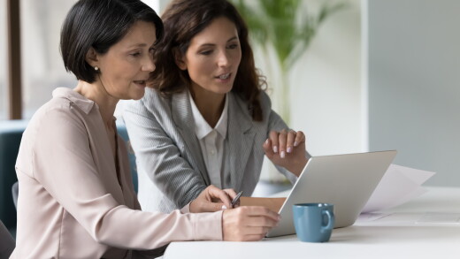 Two businesswomen discuss app or on-line presentation using laptop