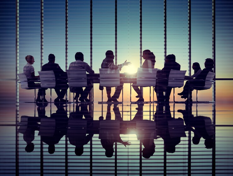 A group of office workers in glass conference room, the sun setting behind them.