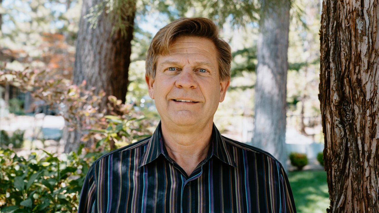 Chris Lewis stands in front of tree trunks.