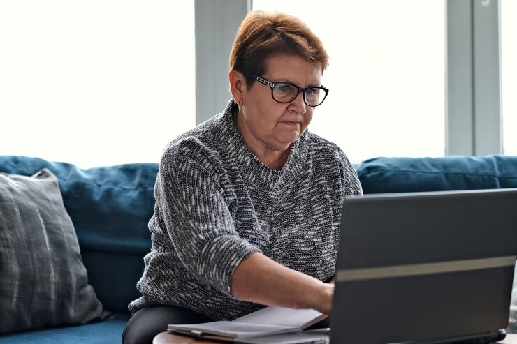 Older woman working on laptop; holding notebook