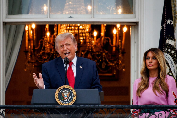 President Trump speaks at an outdoor White House lectern with a lit chandelier in the background, with Melania Trump in a pink dress standing behind him.