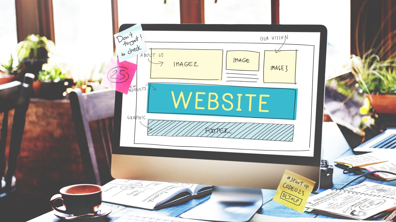 A sketch on a computer monitor surrounded by notebooks, laptops and post-it notes in an office reads "website," symbolizing business website strategy