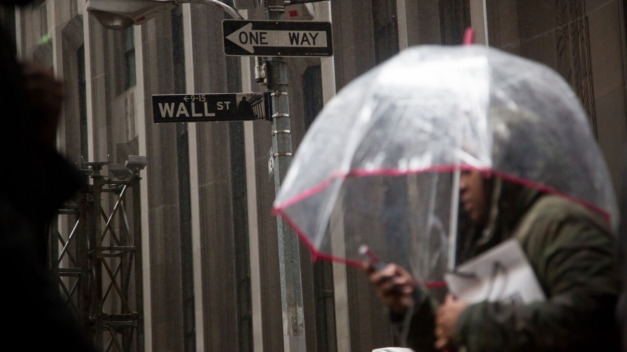 A pedestrian carries an umbrella while walking along Wall Street near the New York Stock Exchange.