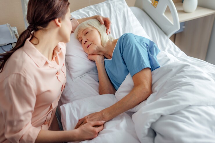 Younger woman sitting in hospital with older woman in hospital bed, holding her hand