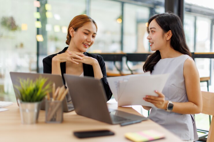 Two women talking, one showing something on paper to another