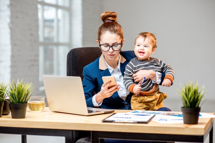 Woman working at her desk while holding a baby.