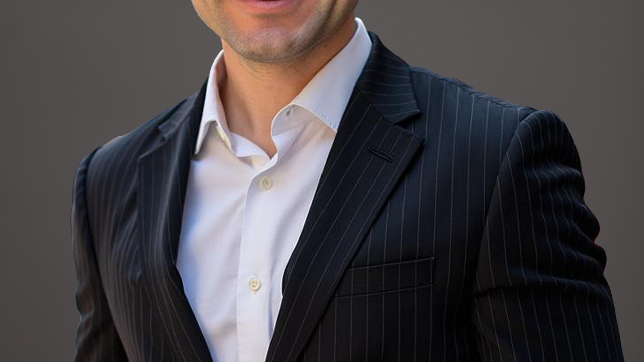 A man dressed in a blazer smiling for a photo.