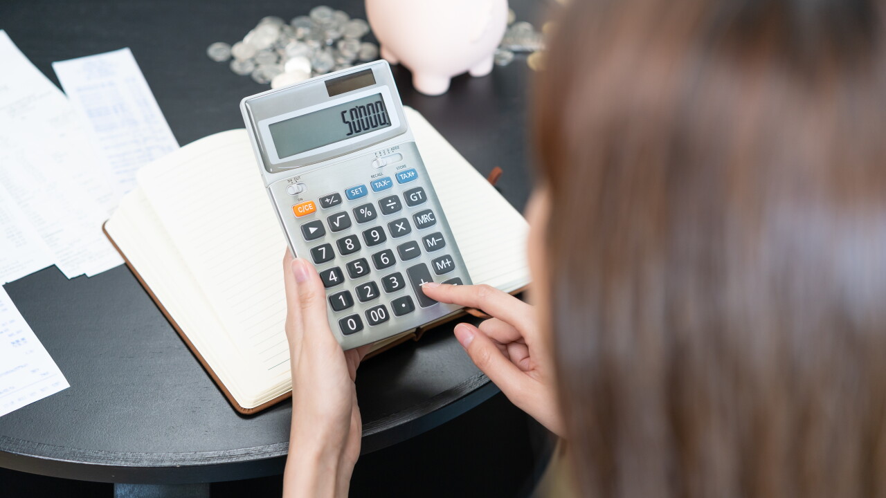 Woman typing on calculator, money and piggy bank on table