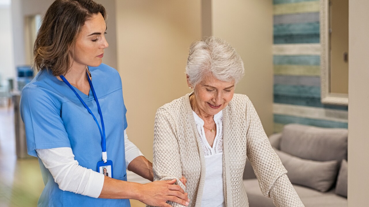 Stock photo of an elderly person with using a walker with assistance from a woman wearing medical scrubs