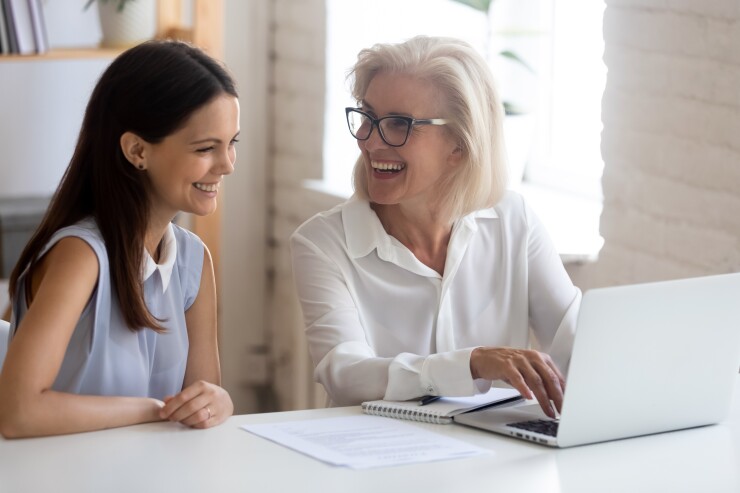 Older employee with younger employee, working on laptop and laughing