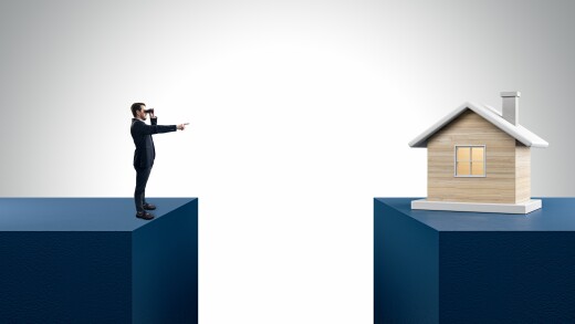 Businessman with telescope pointing at wooden house divided by gap on light background. Mortgage and loan concept.