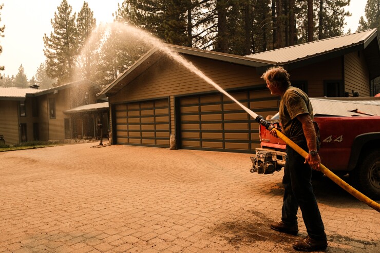 A person hoses a home as a preventative measure during a wildfire