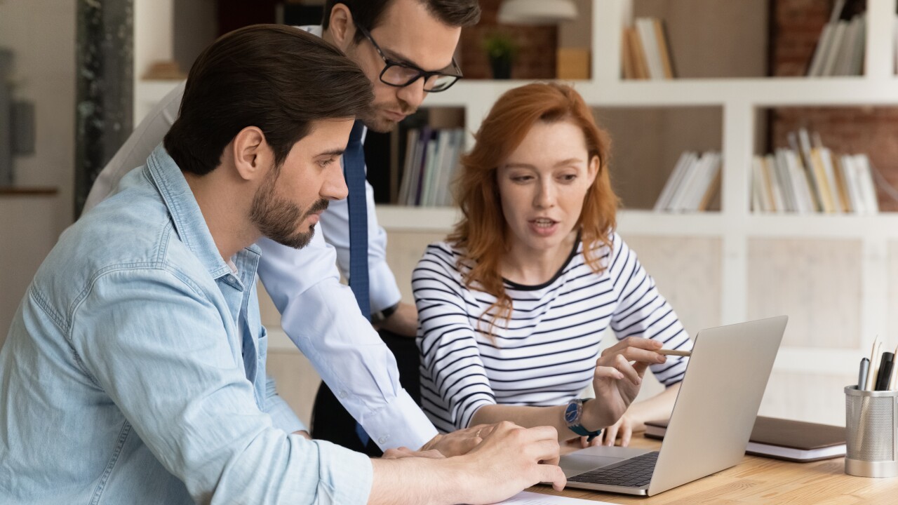 Three employees sitting talking looking at laptop