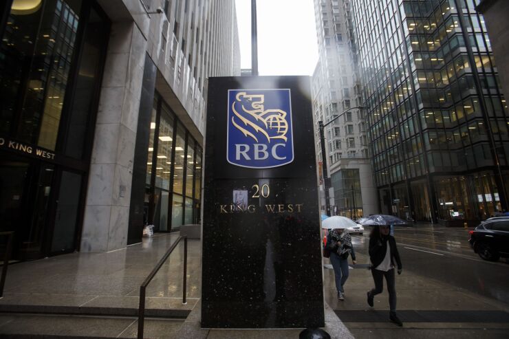 Pedestrians carry umbrellas while walking past Royal Bank of Canada (RBC) signage displayed at the Royal Bank Building during the company's annual general meeting in Toronto, Ontario, Canada, on April 6, 2017. RBC Chief Executive Officer David urged lawmakers to coordinate interventions and act quickly to cool housing markets, particularly in Toronto and Vancouver. Photographer: Cole Burston/Bloomberg