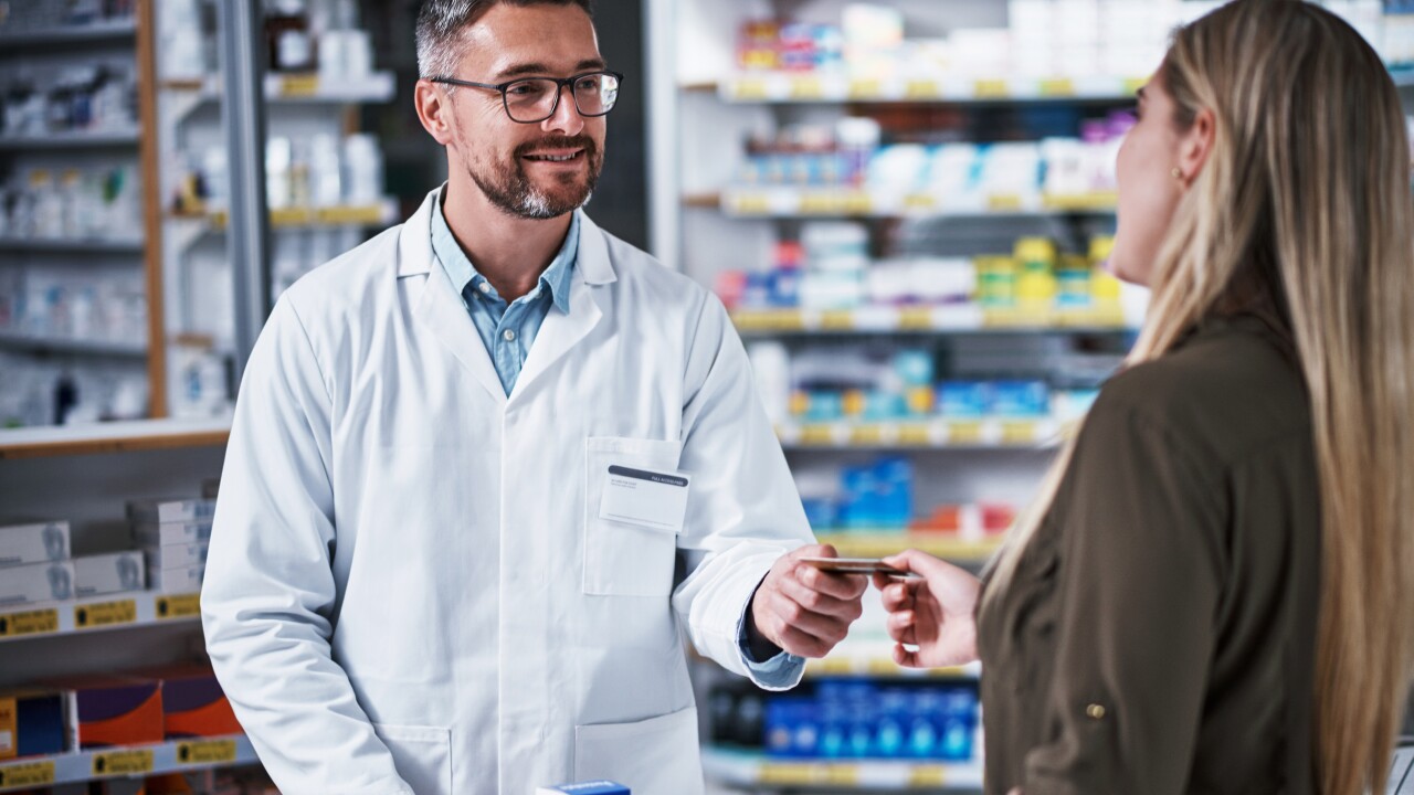 Woman handing pharmacist card, standing at pharmacy counter