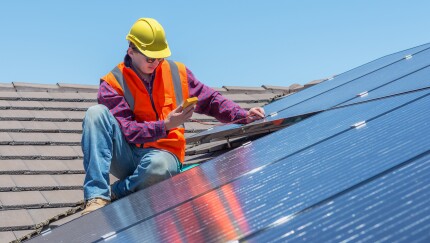 Worker atop a roof covered in solar panels.