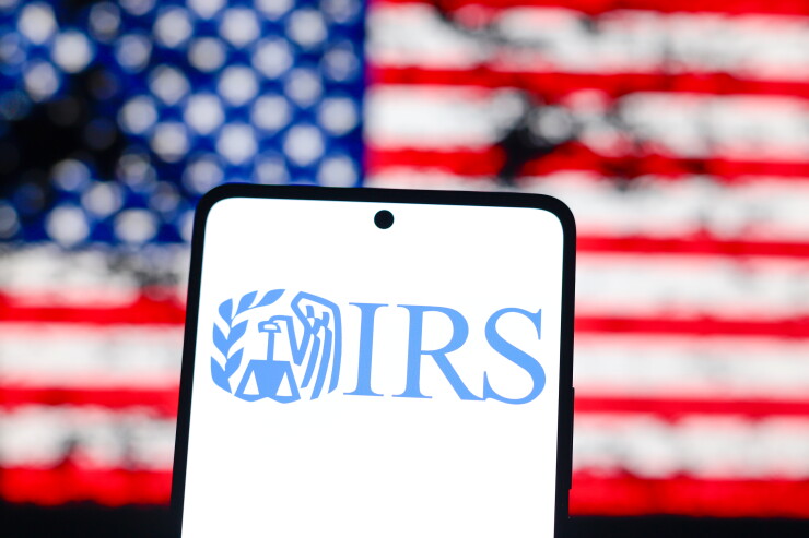 In this photo illustration, the IRS logo is displayed on a smartphone screen and in the background the flag of the United States