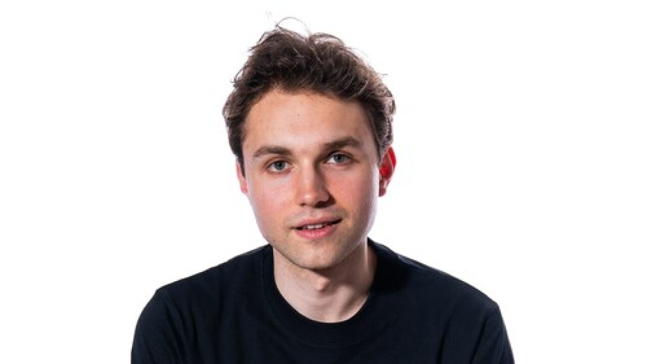 A young man with light brown hair and a black t-shirt posing against a white background.