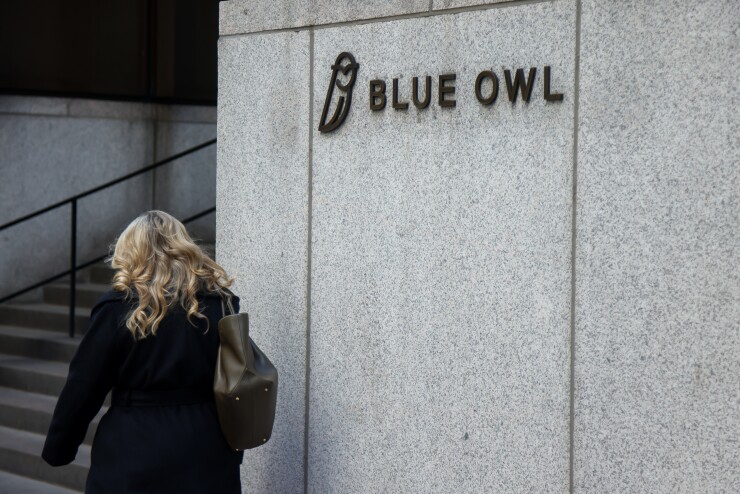 A person walking by the signage for Blue Owl Capital in New York.