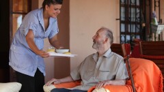 nurse or helper in residential home giving food to old senior man