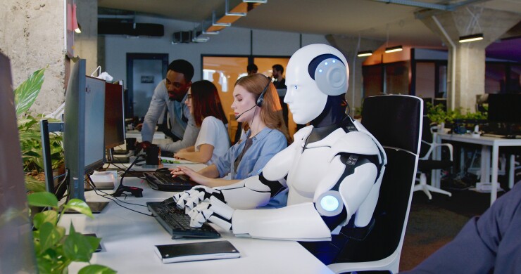 Robot working at computer among people.