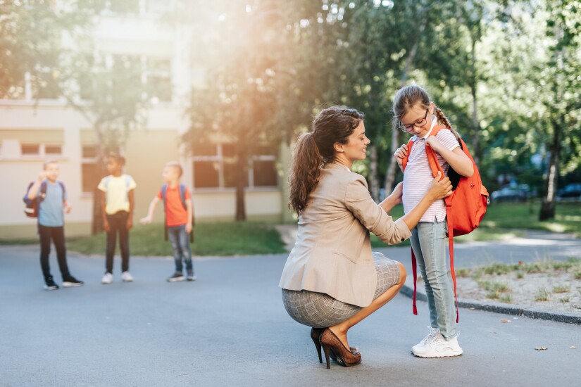 Mom helping daughter with backpack in front of school
