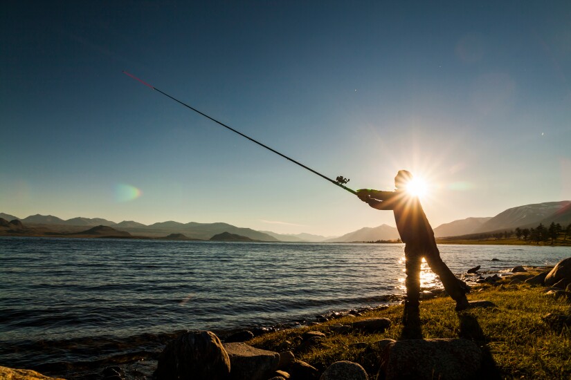 Silhouette of a fisherman at sunset. Fishing on mountain lake