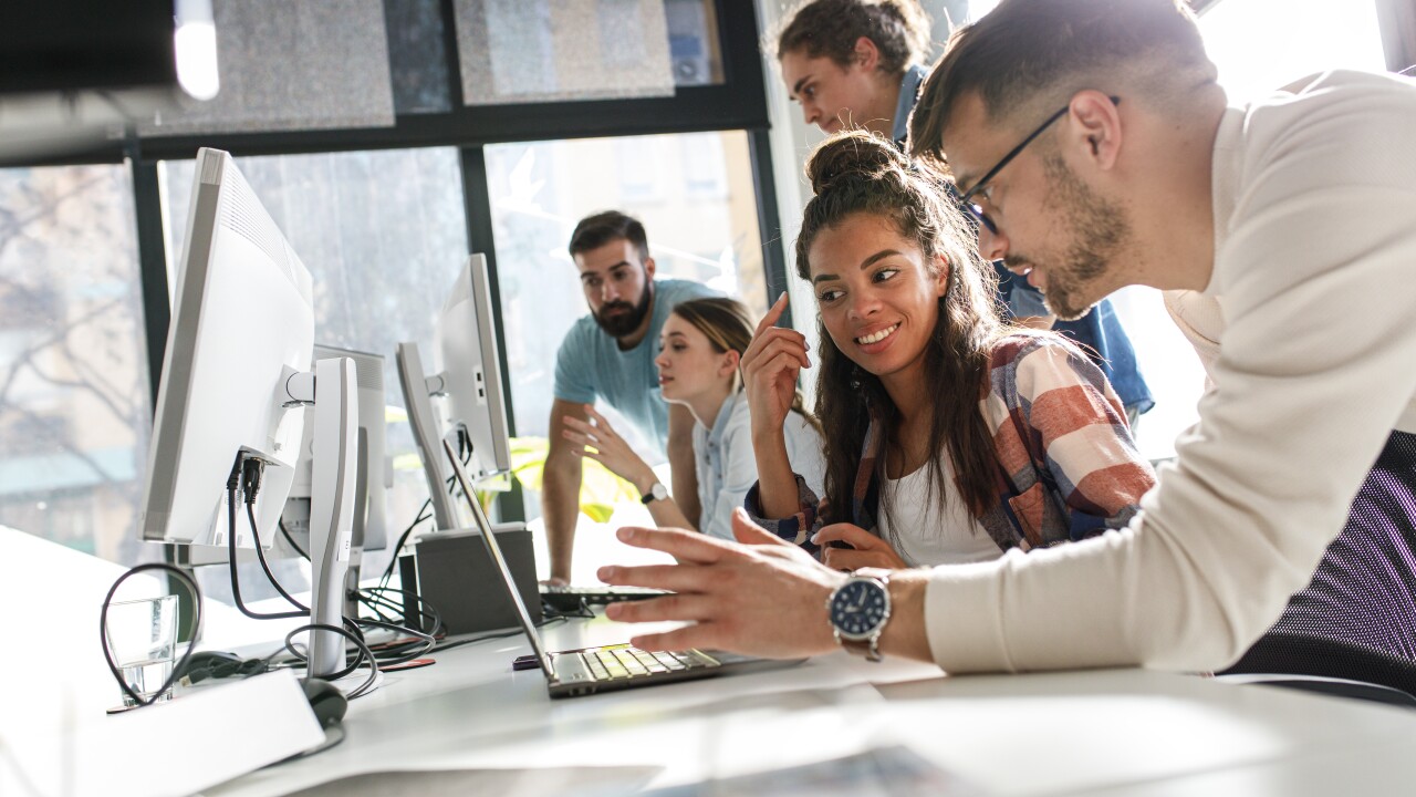 Young employees working together at long desk with computers