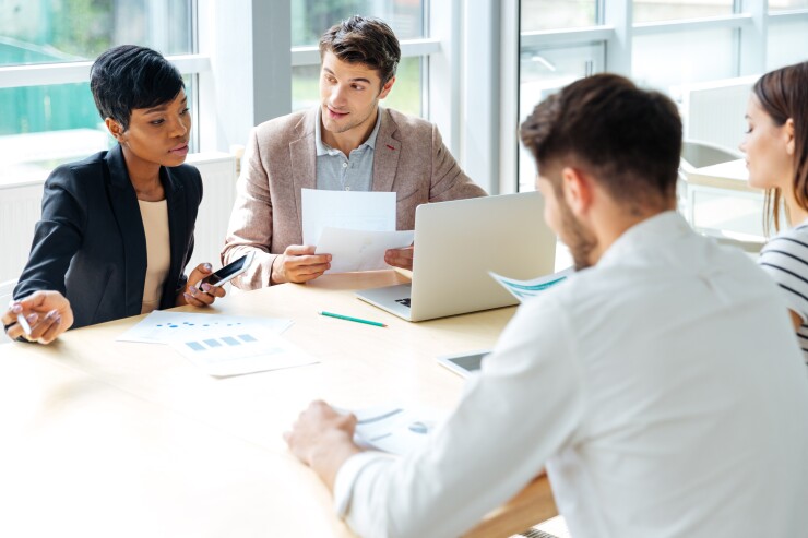Employees sitting around table working, one with laptop