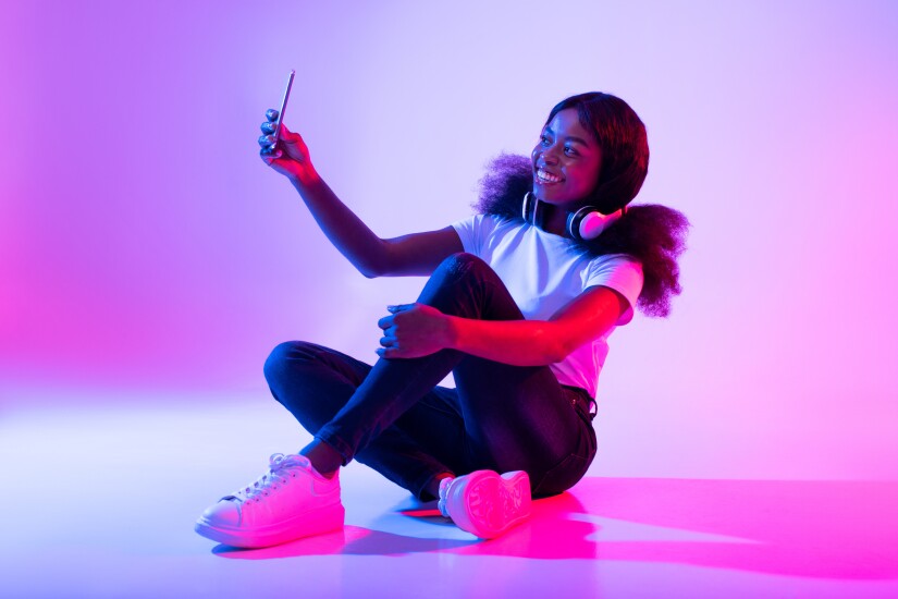 Photography concept. Smiling young black woman taking selfie in neon light, full length