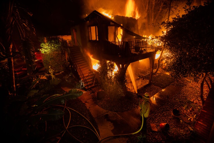 A firefighter hoses down a burning house in Altadena, California.