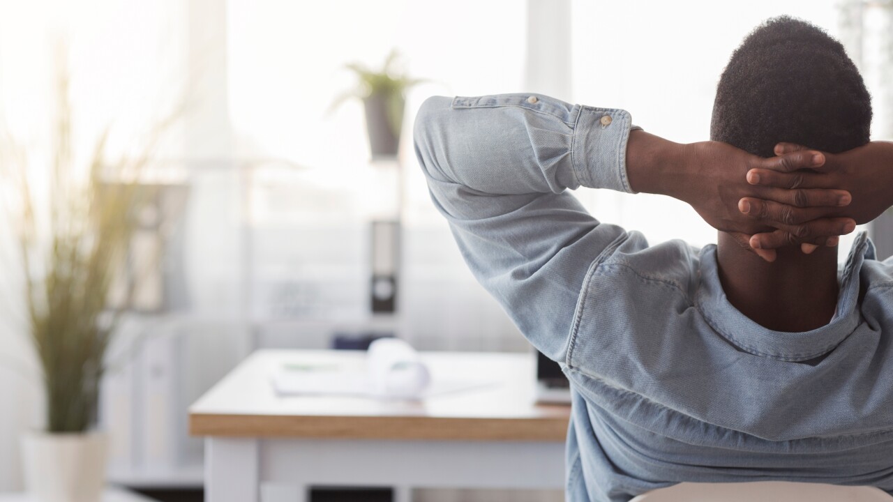 A man leans back on his chair in a sunlit office with plants.