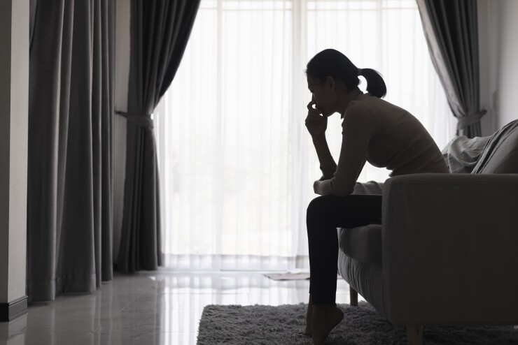 The silhouette of a woman sitting on her couch, deep in thought, alone.