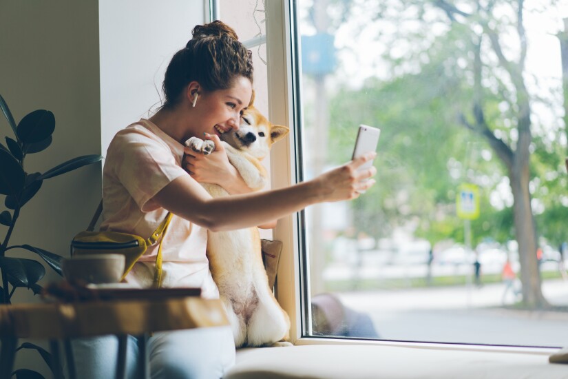 Cheerful lady taking selfie with doggy in cafe using smartphone camera
