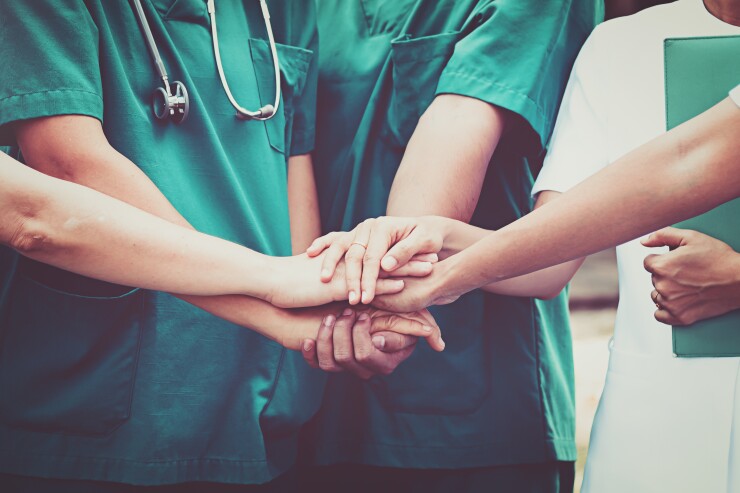 Nurses place their hands on top of each other, in a show of teamwork.