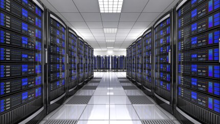 Two rows of computer servers with an aisle down the middle, in an enclosed building with no windows.