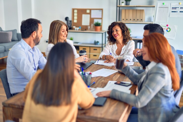Group of employees talking and smiling around conference table