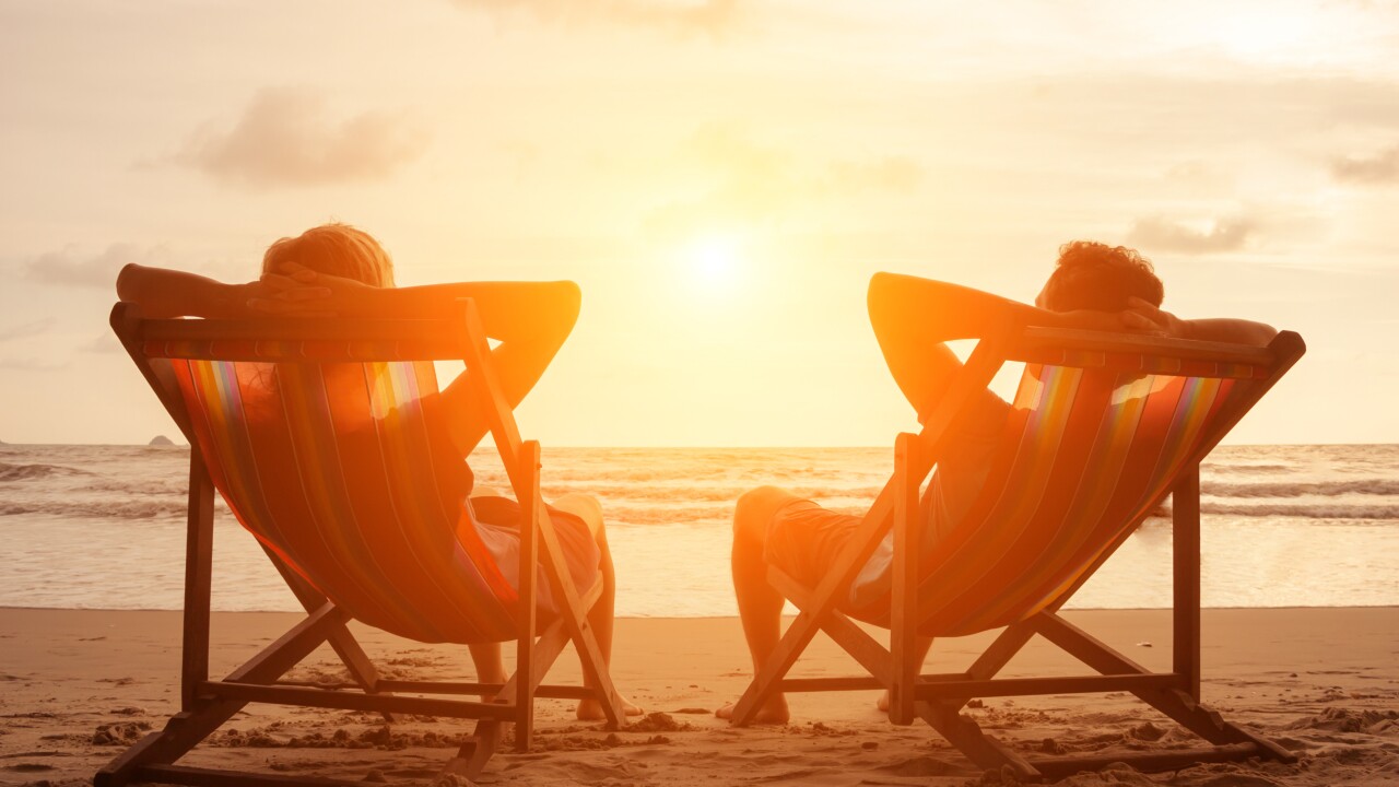Romantic holiday travel. Silhouette of happy young couple sitting in deck chairs in luxury beach hotel at sunset near the sea. Love and relationship concept. Summer vacation in tropical paradise island.