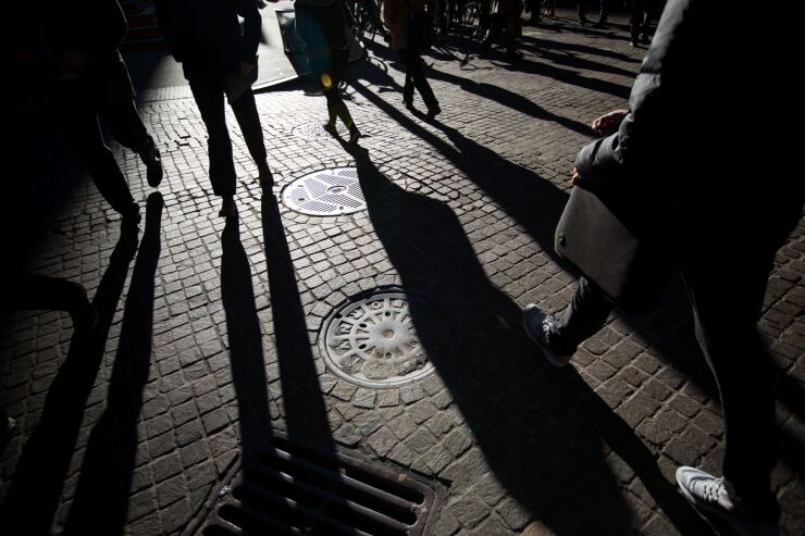 People's feet walking away on dark brick road, shadows behind them