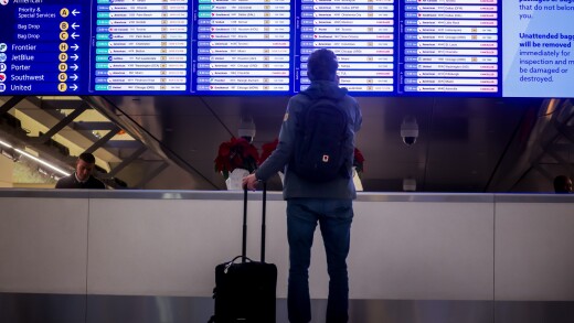 A traveler with a suitcase stands in front of a departure sign board in La Guardia airport.