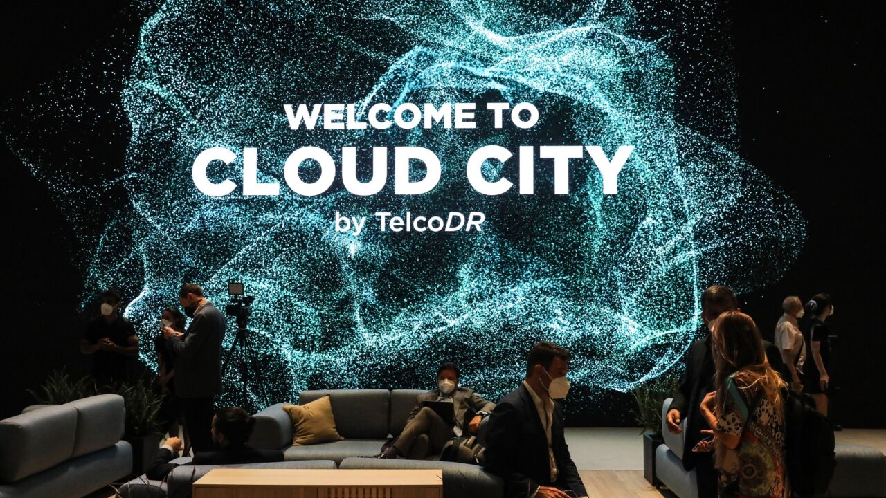Attendees gather beneath an illuminated 'Cloud City' sign on the TelcoDR Inc. stand during the opening day of the MWC Barcelona at the Fira de Barcelona venue in Barcelona, Spain, on Monday, June 28, 2021. MWC Barcelona, which in 2019 attracted 109,000 attendees from 198 countries, was one of the first major European conference casualties due to the pandemic when it was axed in February last year. Photographer: Angel Garcia/Bloomberg