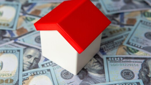 A toy house on a bed of one hundred U.S. dollar bills. Real estate, home finance, mortgage, or property investment concept.