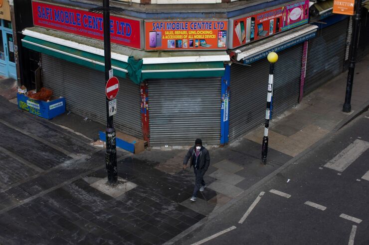 A man in a protective face mask walks past a shuttered store in the Brixton district of London on April 4, 2020
