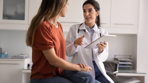 Professional Latina therapist holding modern digital tablet during conversation with woman patient, accessing electronic health record system, explain treatment plan or health test results.