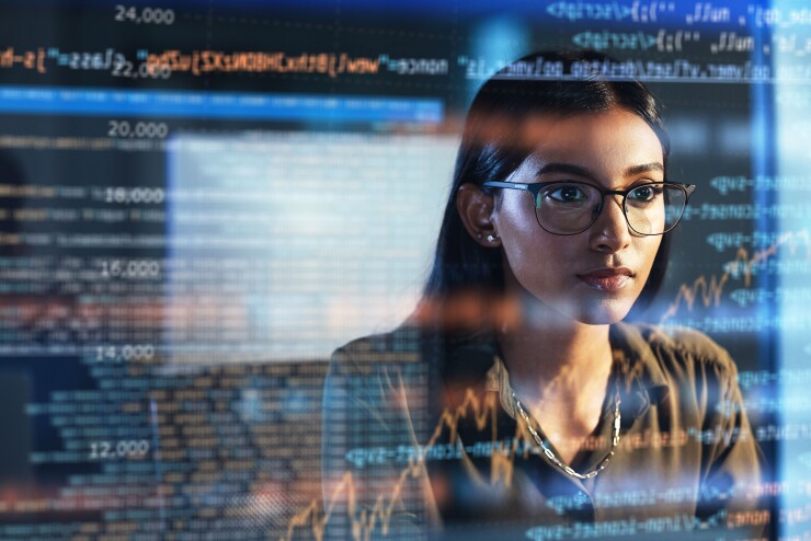 A person sitting at a desk looking at a computer with holographic script overlayed.