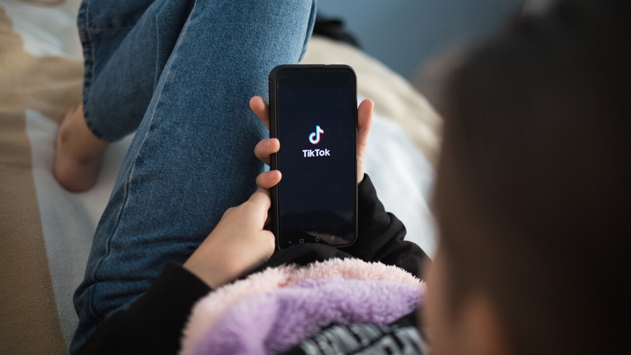 A woman holding her phone, with the app TikTok open.